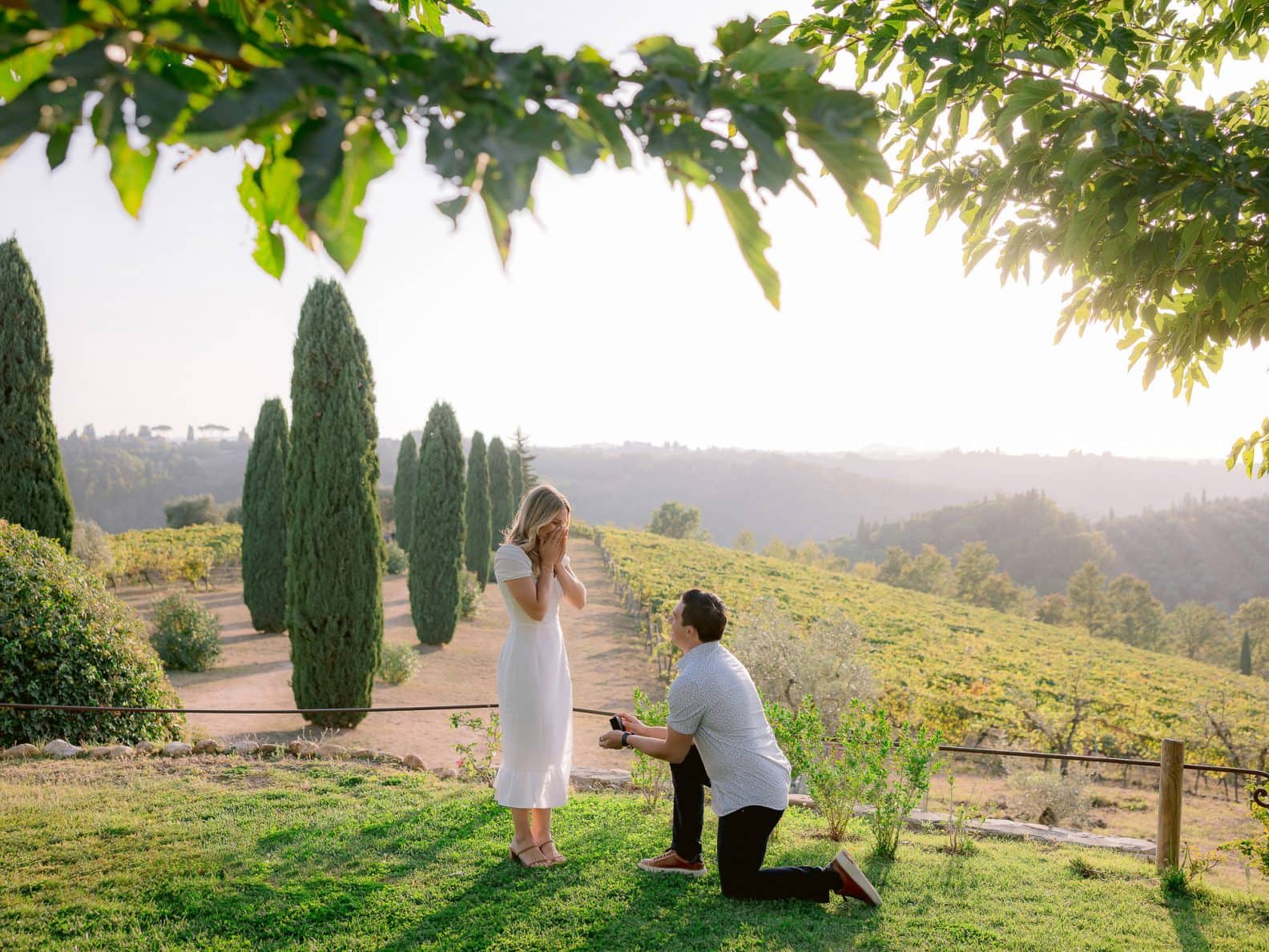 boy kneel down to propose his girlfriend with the tuscan countryside as the backdrop
