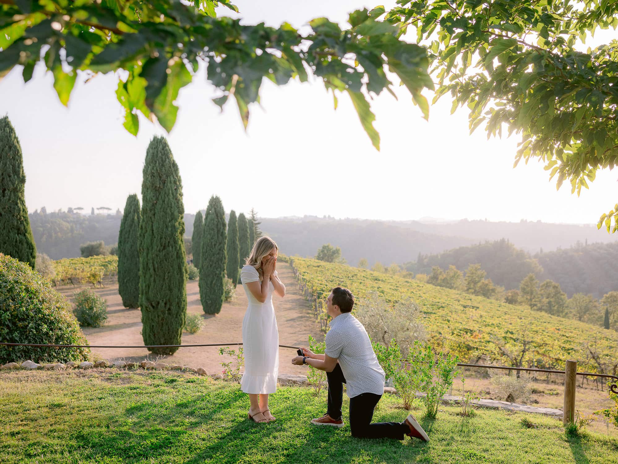 boy kneel down to propose his girlfriend with the tuscan countryside as the backdrop