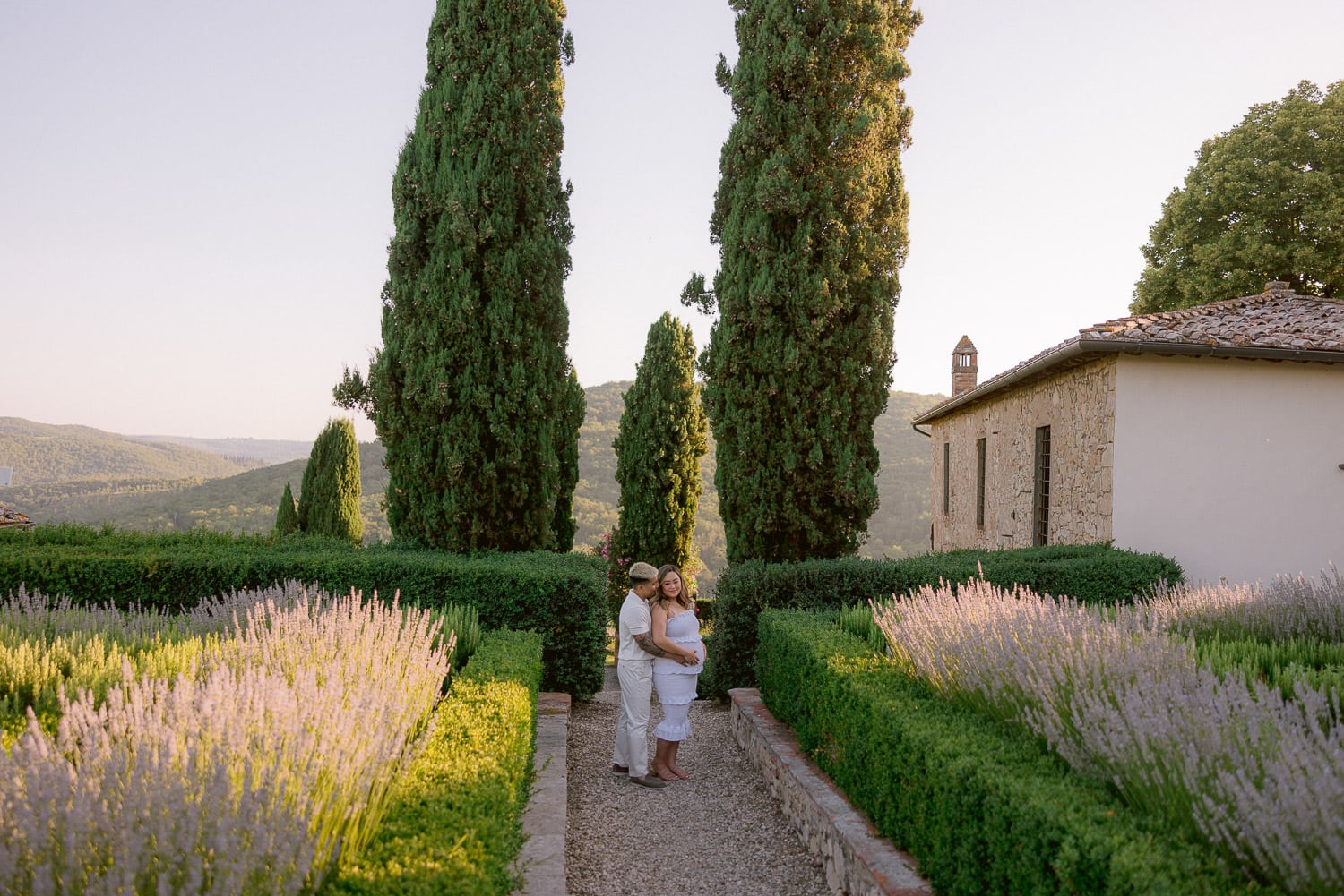 newlyweds expecting their baby posing for the babymoon photographer in the garden of meleto castle with cypress trees and lavender all around